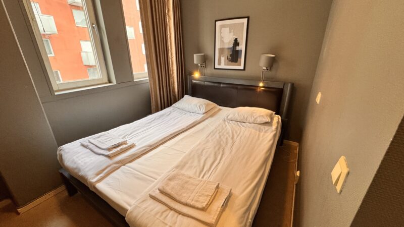 Kompakt dubbelrum på Hotel Expo i Stockholm med två enkelsängar, mjuka färger och fönster med insyn – för dig som söker ett enkelt och prisvärt boende.