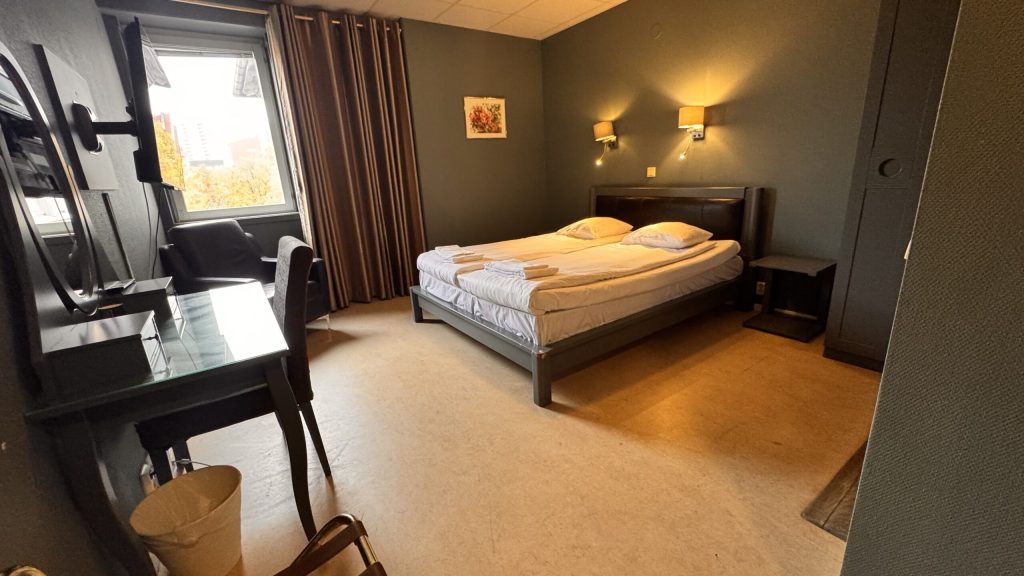 Kompakt dubbelrum standard på Hotel Expo i Stockholm med två enkelsängar, mjuka färger och fönster med insyn – för dig som söker ett enkelt och prisvärt boende.